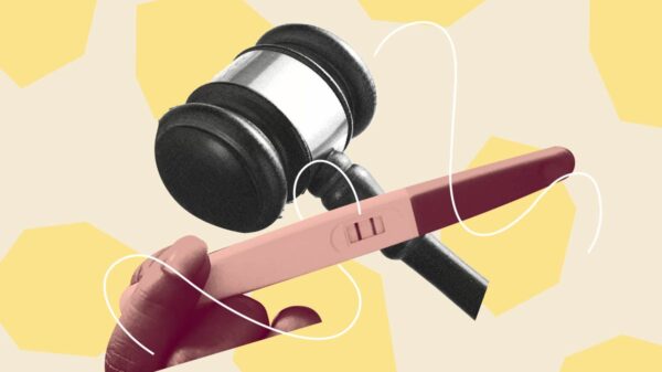 Pink hand holding a pregnancy test over a black and white gavel. Background is beige with light yellow geometric shapes