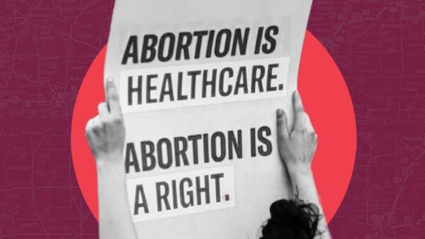 Maroon background, Hands holding sign that says "Abortion is Healthcare. Abortion is a Right" in front of a red circle