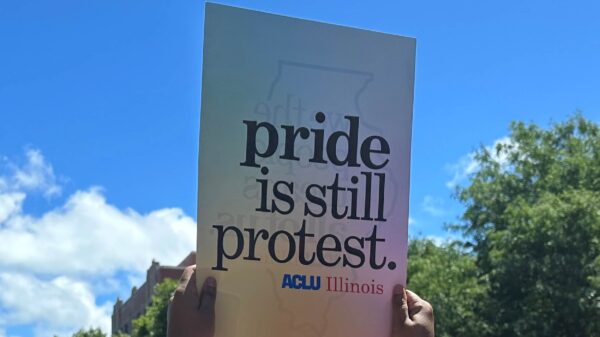 hands holding up sign with rainbow background and gray text "pride is still protest"
