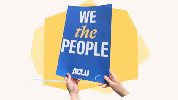 Hands holding blue sign that says "we the people' with yellow shapes behind it.