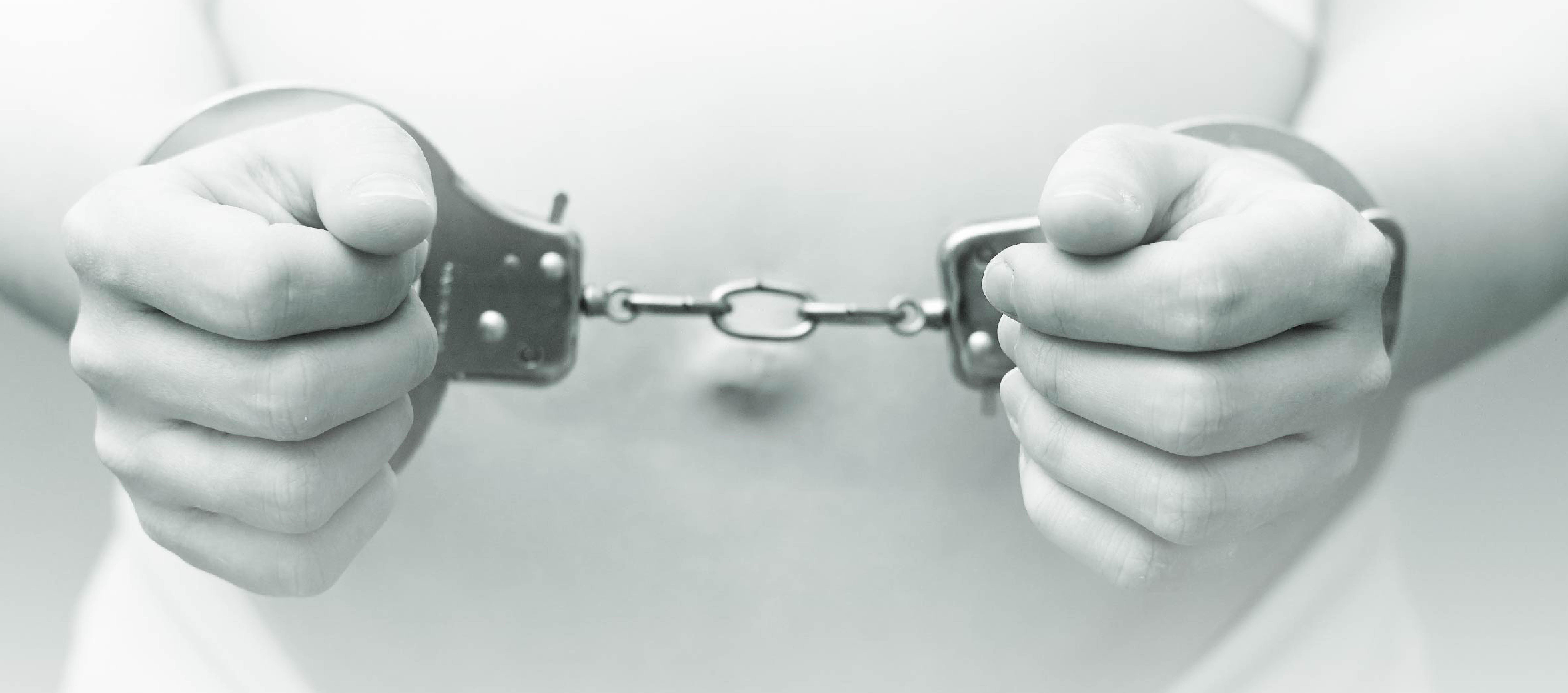 black and white image of a pregnant belly behind hands in handcuffs