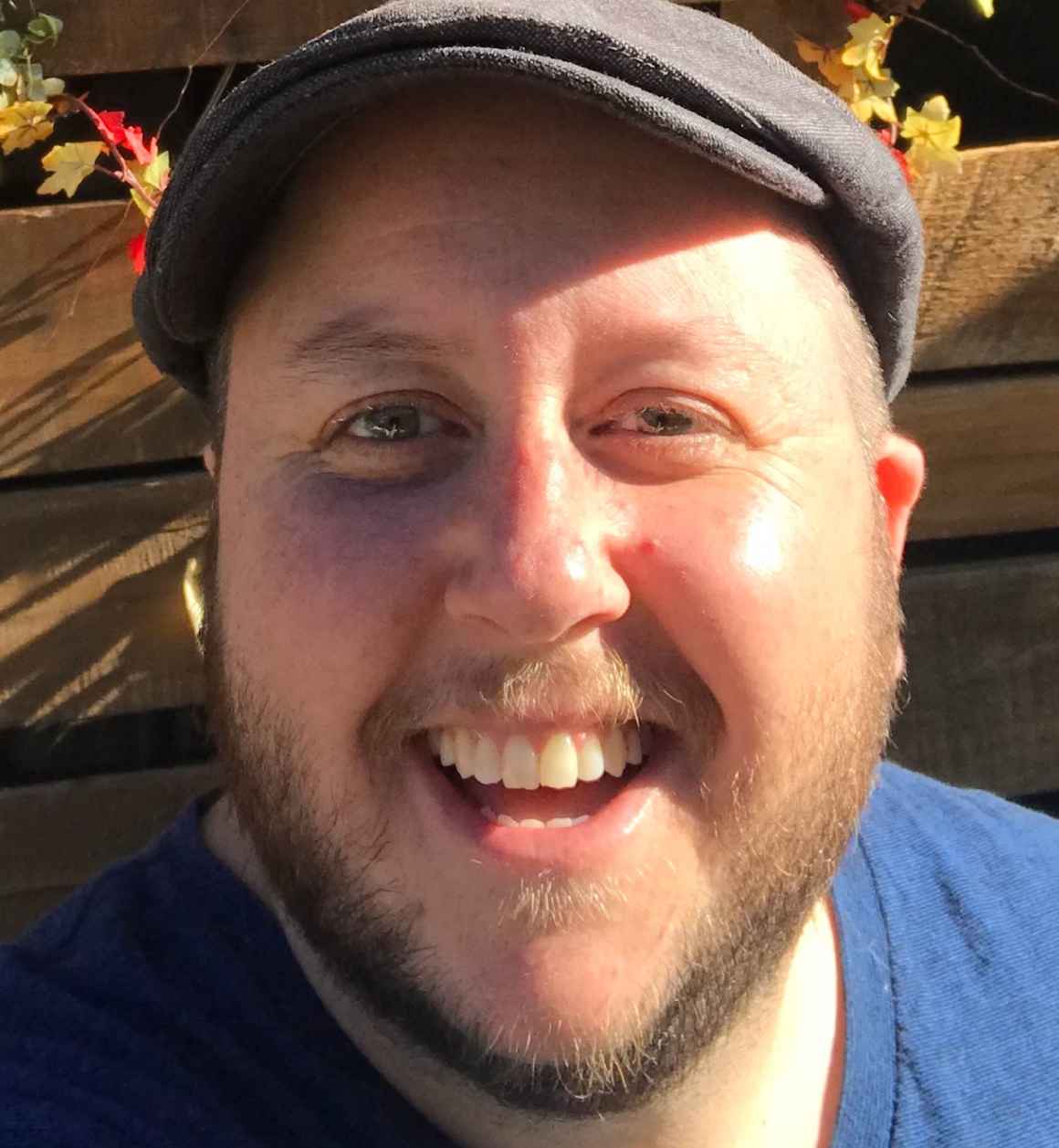 Headshot of Avi wearing a gray hate and blue shirt